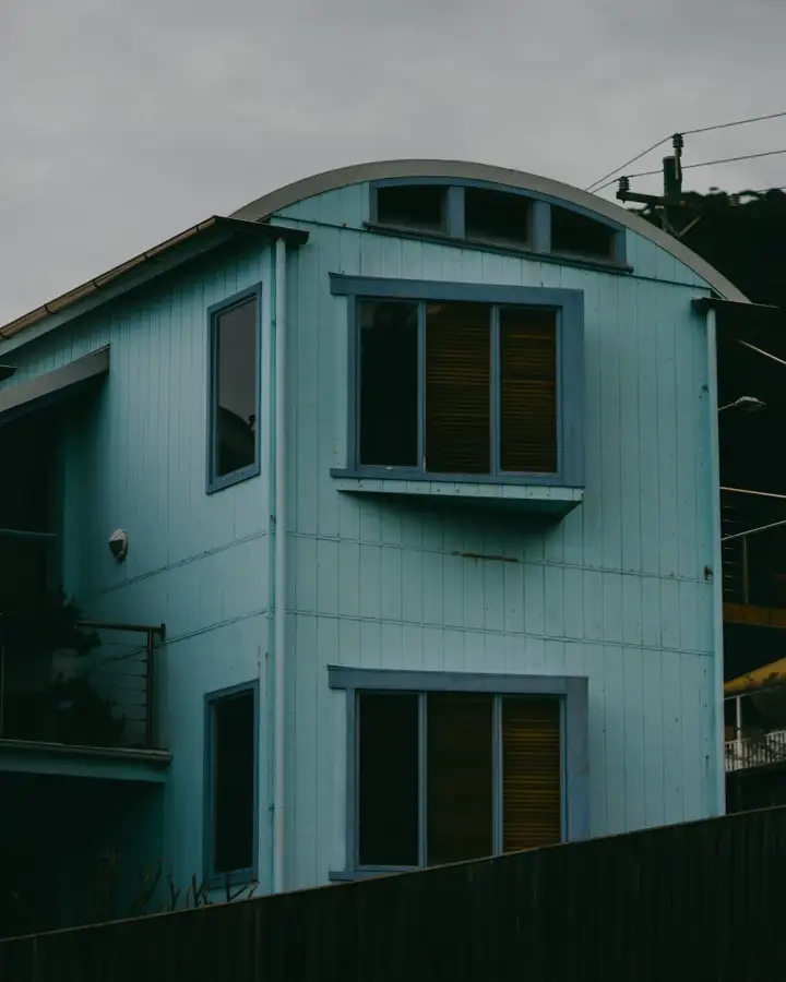 A pale blue timber home with a curved roof on a hillside